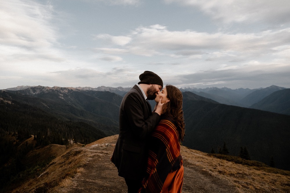 Couple kissing on top of a mountain range with stunning panoramic views