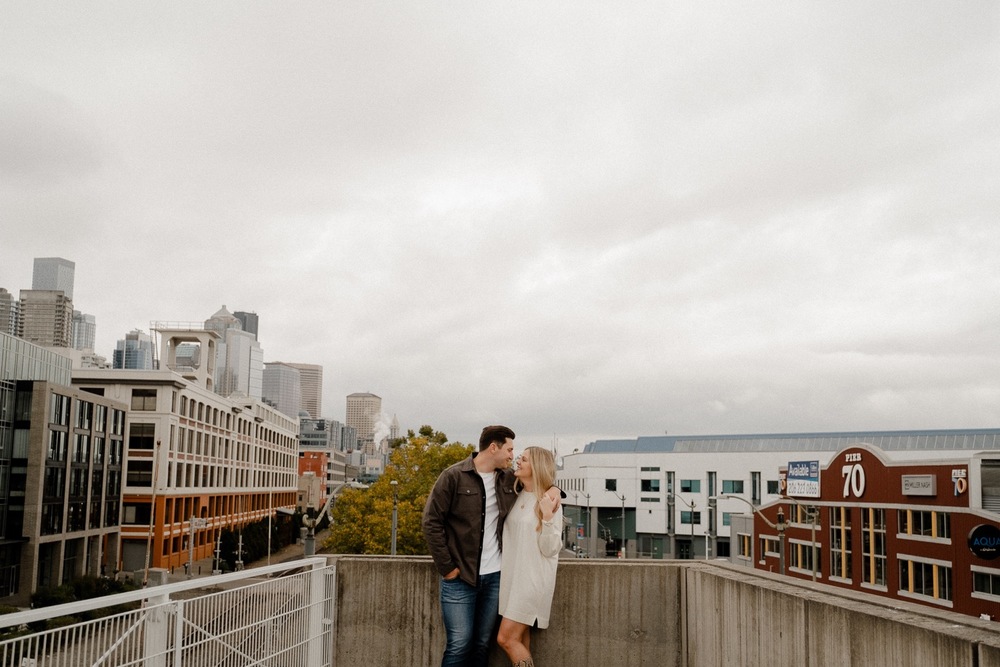 Couple kisses on top of a bridge overlooking downtown Seattle